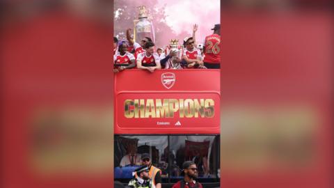 The Arsenal team in open-topped buses holding trophies. Word Champions is written in front of the bus