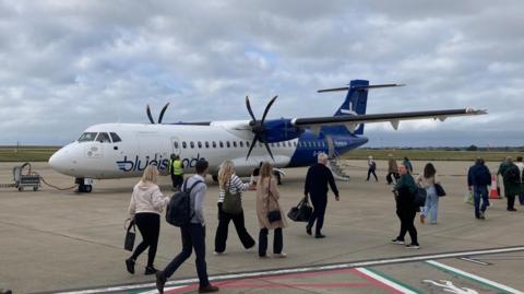 Several passengers walk along the tarmac at an airport as they board a Blue Islands plane.