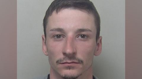 A custody photograph of Jamie Sutton shows a person with short dark hair looking directly at the camera against a plain light-coloured background.