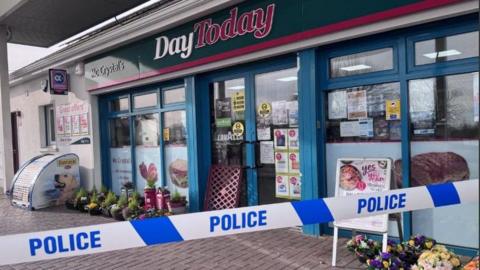 A police cordon can be seen outside a shop. A number of plants can be seen outside it and the words: 'Day Today' are visible on a sign above the shopfront.