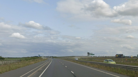 Street view of the A1307. It is a flat stretch of road with a slight bend, but a clear view up ahead. There are two lanes and to the right of the road is a barrier separating traffic moving in the opposite direction.