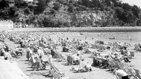 Many people sit on a beach in the sun.