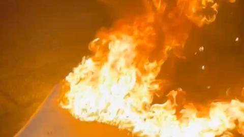 Flames engulf a mattress by the side of the road.