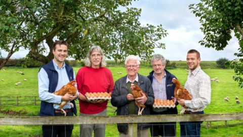 Five men, three holding chickens and two holding eggs