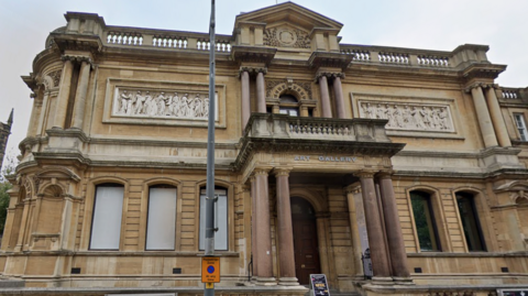 A photo of the exterior of a two-storey Victorian building which has a sign saying 'art gallery on it'. The building has marble pillars.