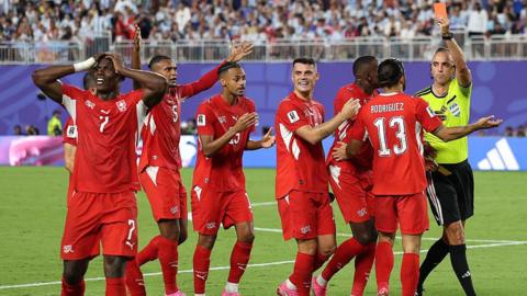 Referee Joao Pinheiro shows a red card to Breel Embolo of Switzerland as his teammate protest the decision