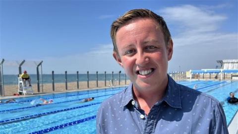 A man smiles at a pool on a sunny day. 