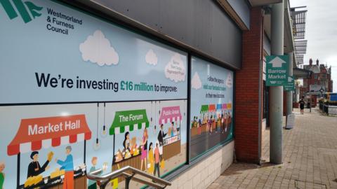 The windows at Barrow Market displaying colourful posters explaining that £16m is being invested in the Market Hall, The Forum and public areas.