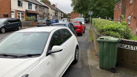 Cars parked on a pavement outside a row of houses