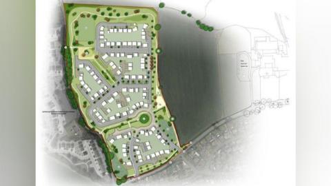 An aerial diagram of the housing development. It is on green lane, with trees and bushes surrounding it. There are 150 white blocks to represent houses, and roads and fields surrounding the site