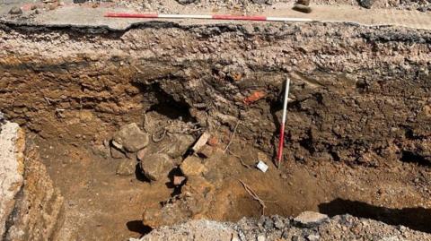 Archaeology trench, showing pieces of stone and red and white distance poles