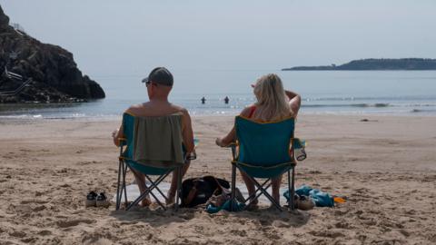 Two people on chair sitting on a beach. They are looking out at the sea. 