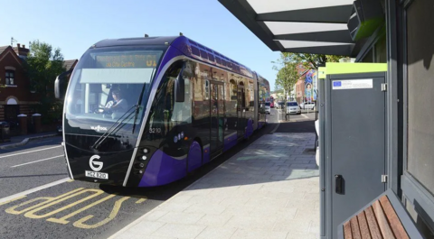 A Translink Glider bus at a stop in Belfast on a sunny day.