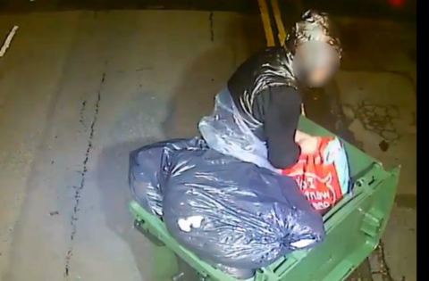 A man in man dressed in a bin bag coming out of the green bin.