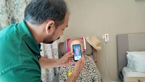 A carer using his smartphone app called Paincheck to monitor a resident's face to check for pain