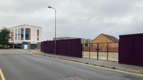 An expanse of fenced off empty grassland with locked double gates on the side of a road.