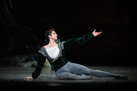 Reece Clarke performs on stage wearing a green velvet top and grey ballet tights. 