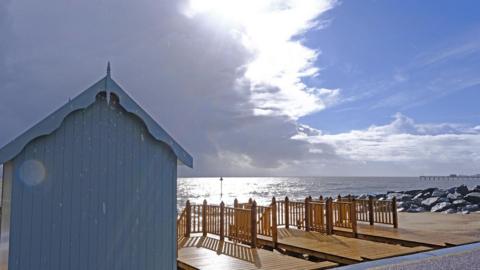 Grey cloud moving over the coastline with a grey beach hut and rocks beneath.