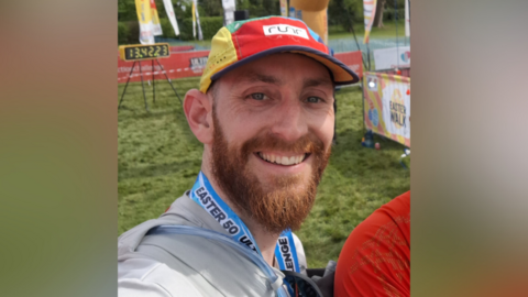 Matt Ireland has a ginger beard and is wearing a colourful cap whilst smiling. The image is a selfie.