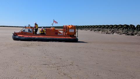 RNLI Hoylake's hovercraft on New Brighton beach on a sunny day as the Coastguard and RNLI rescue a woman. 