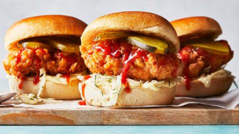 Three Korean-style fried chicken burgers on a wooden chopping board. 