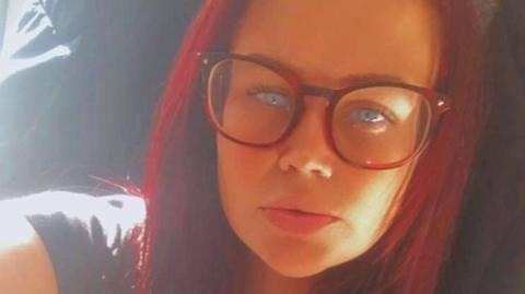 A woman with red hair and glasses in a selfie.