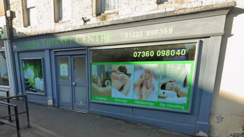 A Google Map image of a grey painted shopfront which has massage images on it - such as hands holding a foot, hands massaging a back and a woman with her head tilted to the side. In green, it reads 'Sakura Therapy Centre'