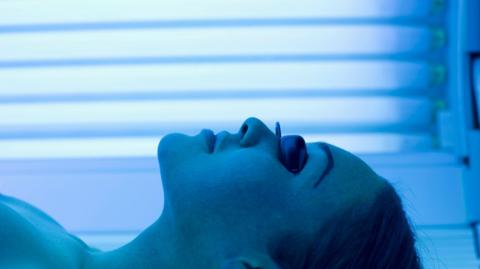 A woman with black goggles on lies in a sunbed under ultra-violet light.