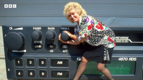 Gloria Hunniford holding the dial of a large prop radio.