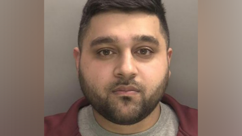 Police mugshot of Mohammed Nafees Ahmed, who is wearing a grey t-shirt and red jacket