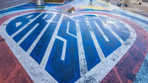 A large heart painted in red, white and blue on a pavement in a shopping centre, with the word 'Bristol' in the middle, in the shape of the heart