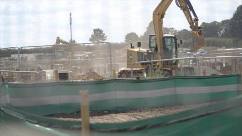 The image shows a construction site where two excavators can be seen, as well as a lot of dust in the air.