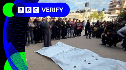 People standing over three bodies laid out on the floor