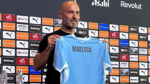 Enzo Maresca holding up a Man City shirt at his first news conference