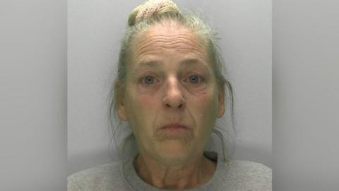 Mug shot of Donna Green. She has her grey hair up in a bun and is wearing a grey shirt. 