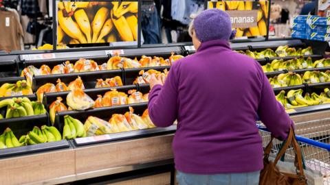 A woman in a purple jumper shops for bananas in a supermarket in the UK