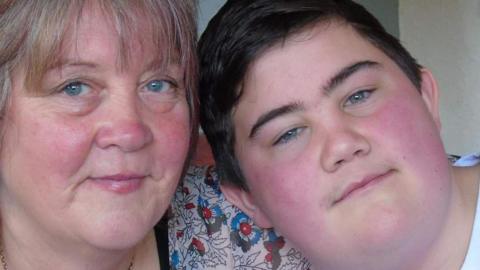 A woman and a boy pose for a photo, the woman is wearing a floral patterned top.