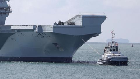 Royal Navy aircraft carrier HMS Queen Elizabeth being towed by a tug boat