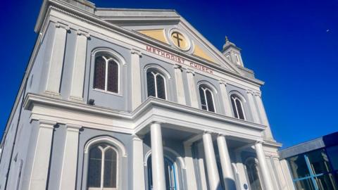 St Helier Methodist Church. A large blue and white building. The sky is blue. 