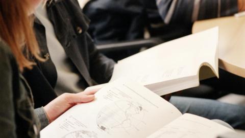 Two students are reading textbooks. In the foreground the book is open on a page with a black and white illustration of the globe.