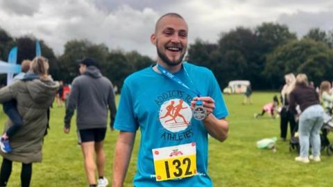 Connor Shannon wearing a blue Addicts to Athletes T-shirt with a race number on the front and holding a medal.