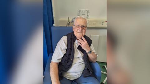 Terry Barraclough sitting in a hospital chair wearing a white T shirt and waistcoat