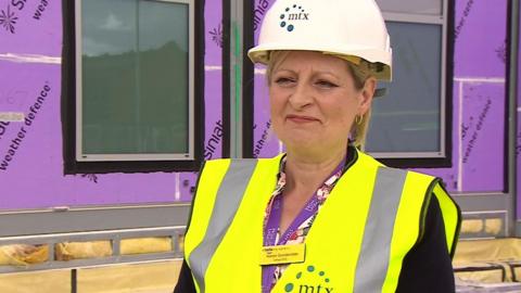 Professor Karen Dunderdale. She is standing outside one of the centres. She is wearing a white hard hat and a fluorescent jacket