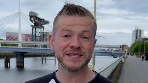 Derek Mac an Tòisich bho sgioba BBC Aimsir taobh a-muigh na h-oifis an Glaschu