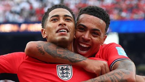 Two black footballers celebrating a goal, wearing red England shirts
