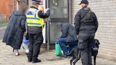 Police officers are searching a suspect for drugs on the streets of Torquay.  A police sniffer dog has identified a suspect. 