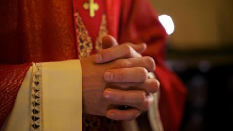 Priest hands clasped together in red robes