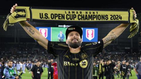 Olivier Giroud holds up a scarf in celebration which says 'Lamar Hunt US Open Cup champions 2024', in the colours of LAFC