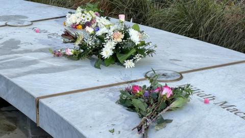 Two bunches of flowers on a marble bench with two names inscribed into it. 