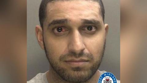 Mugshot of Rahul Sharma. A close-up image of Sharma looking at the camera, his left eye is bloodshot. He wears a grey shirt and stands in front of a grey background. The West Midlands Police logo is at the bottom right of the image.